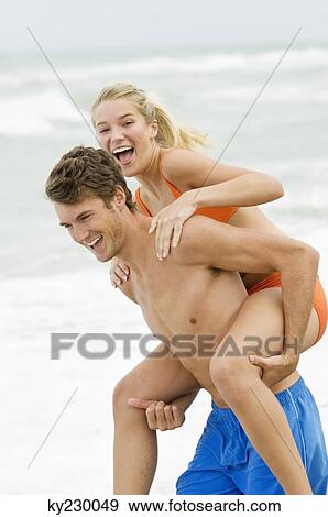 Man giving woman piggyback ride on the beach View Large Photo Image Stock Photo - Man giving woman piggyback ride on the beach. Fotosearch