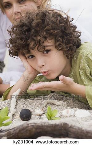 Picture - Boy lying with his mother on the beach. Fotosearch