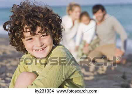 Picture - Boy smiling with his family behind him on the beach. Fotosearch