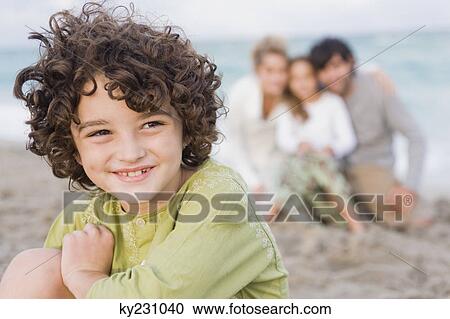 Boy smiling with his family behind him on the beach View Large Photo Image Stock Image - Boy smiling with his family behind him on the beach. Fotosearch