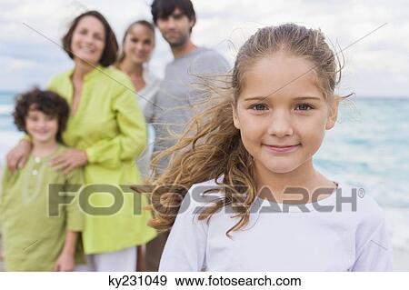 Girl smiling with her family behind her on the beach View Large Photo Image Stock Photo - Girl smiling with her family behind her on the beach. Fotosearch