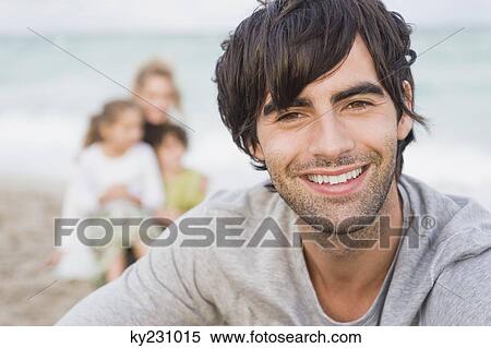 Man smiling with his family behind him on the beach View Large Photo Image Stock Photography - Man smiling with his family behind him on the beach. Fotosearch