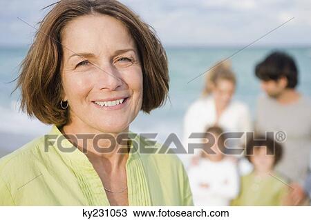 Woman smiling with her family behind her on the beach View Large Photo Image Stock Image - Woman smiling with her family behind her on the beach. Fotosearch
