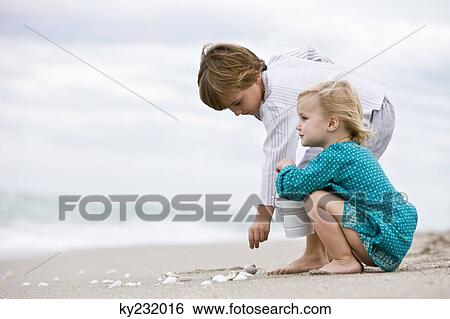 Stock Photograph - Boy and his sister playing with shells on the beach. Fotosearch