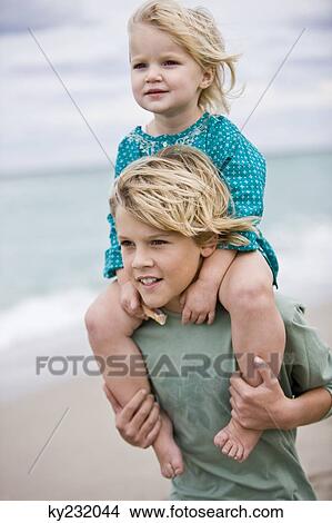 Picture - Boy carrying his sister on shoulders on the beach. Fotosearch