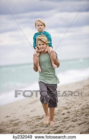 Stock Photo - Boy carrying his sister on shoulders on the beach. Fotosearch