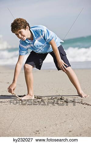 Stock Photo - Boy drawing in sand on the beach. Fotosearch