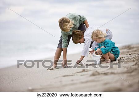 Stock Image - Girl and boys playing with shells on the beach. Fotosearch