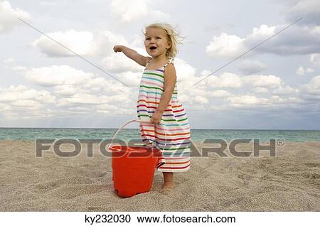 Girl holding a sand pail on the beach and pointing towards the sea View Large Photo Image Stock Image - Girl holding a sand pail on the beach and pointing towards the sea. Fotosearch
