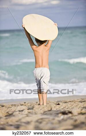 Rear view of a boy holding a body board over his head View Large Photo Image Stock Photo - Rear view of a boy holding a body board over his head. Fotosearch