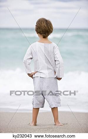 Rear view of a boy standing on the beach View Large Photo Image Stock Image - Rear view of a boy standing on the beach. Fotosearch