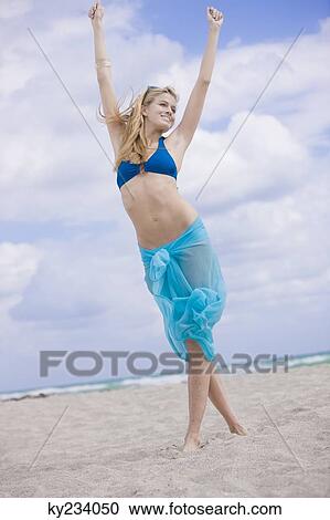 Stock Image - Woman standing on the beach with her arms raised. Fotosearch