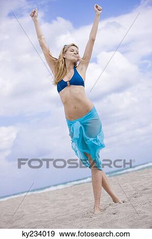 Woman standing on the beach with her arms raised View Large Photo Image Stock Photo - Woman standing on the beach with her arms raised. Fotosearch