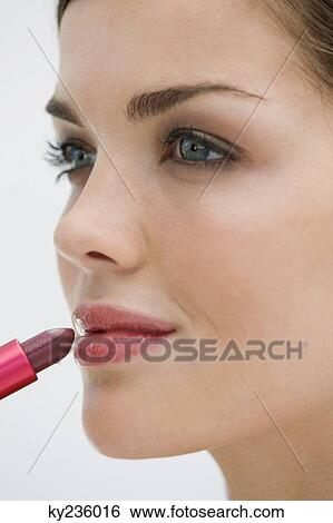 Stock Photograph - Fashion model applying lipstick on her lips. Fotosearch