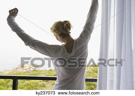 Rear view of a woman stretching her arms in balcony View Large Photo Image Stock Image - Rear view of a woman stretching her arms in balcony. Fotosearch
