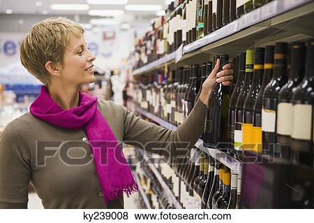 Woman choosing a wine bottle in a supermarket View Large Photo Image Stock Photo - Woman choosing a wine bottle in a supermarket. Fotosearch
