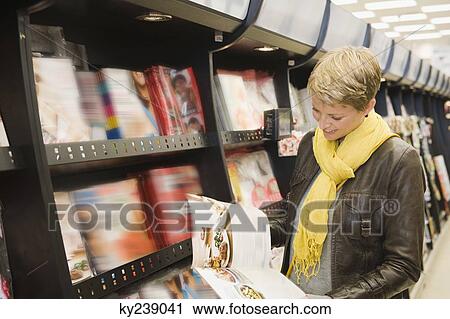 Stock Image - Woman choosing magazines in a supermarket. Fotosearch