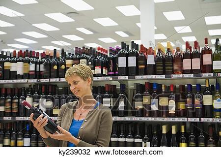 Stock Image - Woman reading a label of a wine bottle. Fotosearch