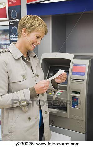 Woman reading a transaction slip at an ATM and smiling View Large Photo Image Stock Photograph - Woman reading a transaction slip at an ATM and smiling. Fotosearch