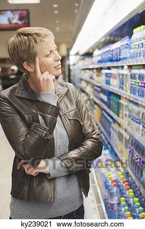 Stock Image - Woman thinking to buy water bottle in a store. Fotosearch
