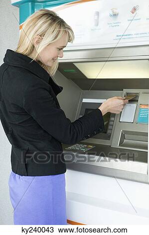 Stock Image - Woman inserting a credit card into ATM. Fotosearch
