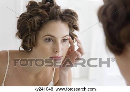 Stock Photo - Woman examining her face in the mirror. Fotosearch