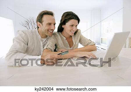 Picture - Couple holding a credit card and working on a laptop. Fotosearch