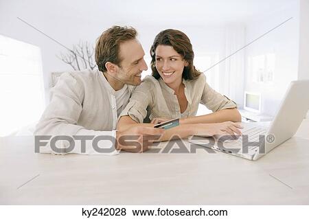 Stock Photo - Couple holding a credit card and working on a laptop. Fotosearch