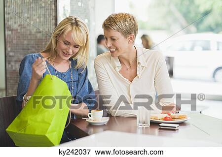 Two women looking in a shopping bag in a restaurant View Large Photo Image Stock Photo - Two women looking in a shopping bag in a restaurant. Fotosearch