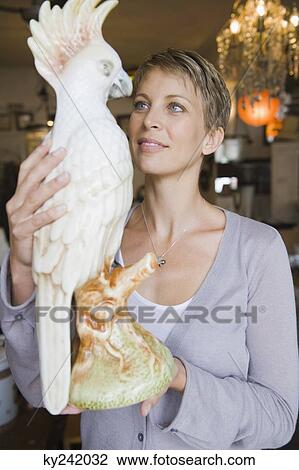 Woman holding a statue of a parrot in a store View Large Photo Image Stock Image - Woman holding a statue of a parrot in a store. Fotosearch