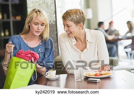 Woman sitting in a restaurant with her friend showing clothes to her View Large Photo Image Stock Photo - Woman sitting in a restaurant with her friend showing clothes to her. Fotosearch