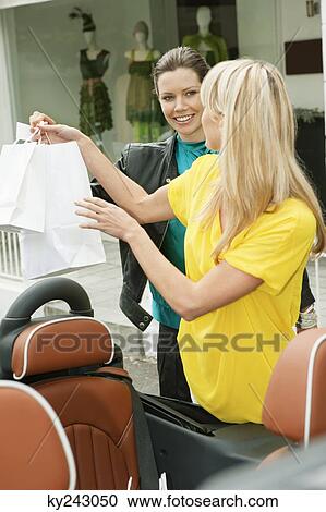 Two women smiling near a car after shopping View Large Photo Image Stock Image - Two women smiling near a car after shopping. Fotosearch