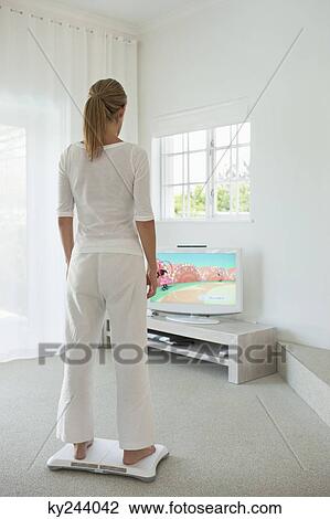 Stock Image - Woman doing step aerobics and watching TV. Fotosearch