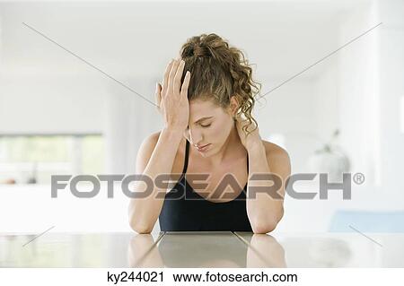 Stock Image - Woman sitting at a table with her head in her hand. Fotosearch