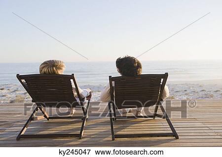 Couple reclining on deck chairs on the beach View Large Photo Image Stock Photo - Couple reclining on deck chairs on the beach. Fotosearch