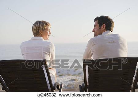 Couple sitting on deck chairs on the beach View Large Photo Image Stock Image - Couple sitting on deck chairs on the beach. Fotosearch