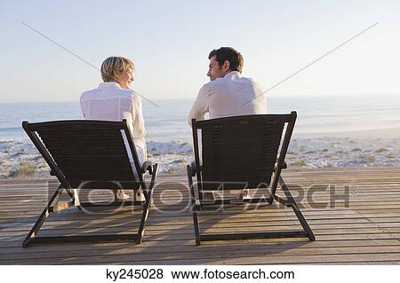 Stock Photo - Couple sitting on deck chairs on the beach. Fotosearch