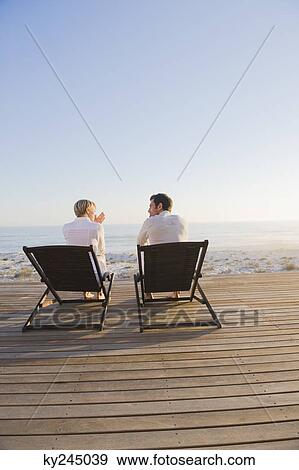 Stock Photo - Couple sitting on deck chairs on the beach. Fotosearch