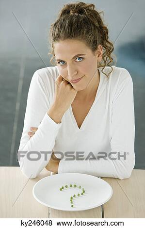 Woman sitting at a table with peas in question mark shape on a plate View Large Photo Image Stock Photo - Woman sitting at a table with peas in question mark shape on a plate. Fotosearch