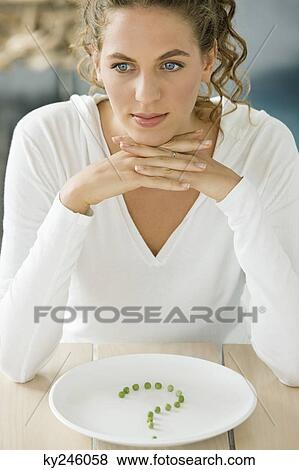 Woman sitting at a table with peas in question mark shape on a plate View Large Photo Image Stock Photo - Woman sitting at a table with peas in question mark shape on a plate. Fotosearch