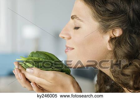 Stock Photography - Woman smelling spinach leaves in the kitchen. Fotosearch