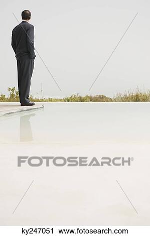 Businessman standing at the poolside and looking at sea view View Large Photo Image Stock Image - Businessman standing at the poolside and looking at sea view. Fotosearch