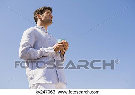Man holding a cup of coffee on the beach View Large Photo Image Stock Image - Man holding a cup of coffee on the beach. Fotosearch