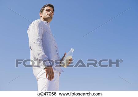 Stock Photograph - Man holding milk bottle on the beach. Fotosearch