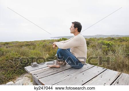 Picture - Man sitting on a boardwalk and thinking. Fotosearch