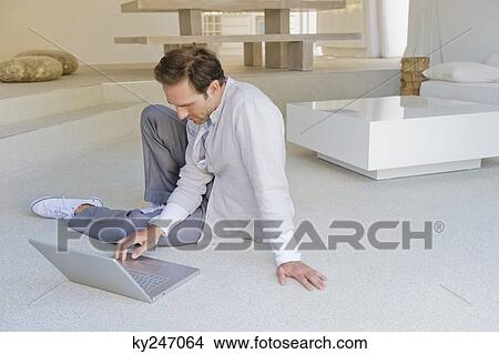 Man sitting on the floor and working on a laptop View Large Photo Image Picture - Man sitting on the floor and working on a laptop. Fotosearch