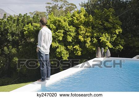 Stock Image - Man standing at the poolside. Fotosearch