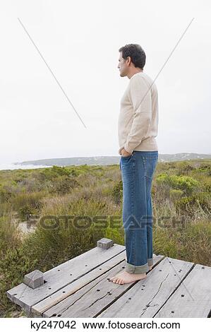 Stock Image - Man standing on a boardwalk and thinking. Fotosearch