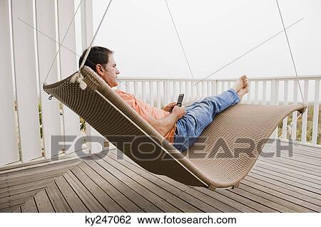 Stock Image - Man using a mobile phone on a porch swing. Fotosearch