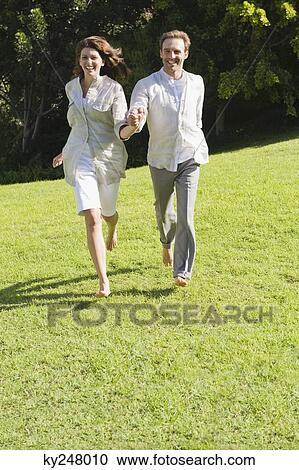 Stock Image - Couple running on grass. Fotosearch